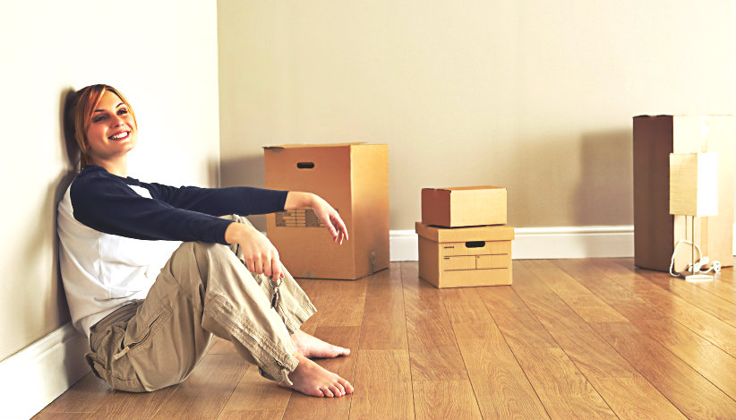 smiling young lady sitting on the floor with some packed boxes around