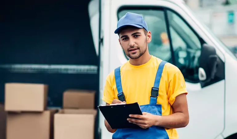 young professional with a notepad standing with a van containing some boxes