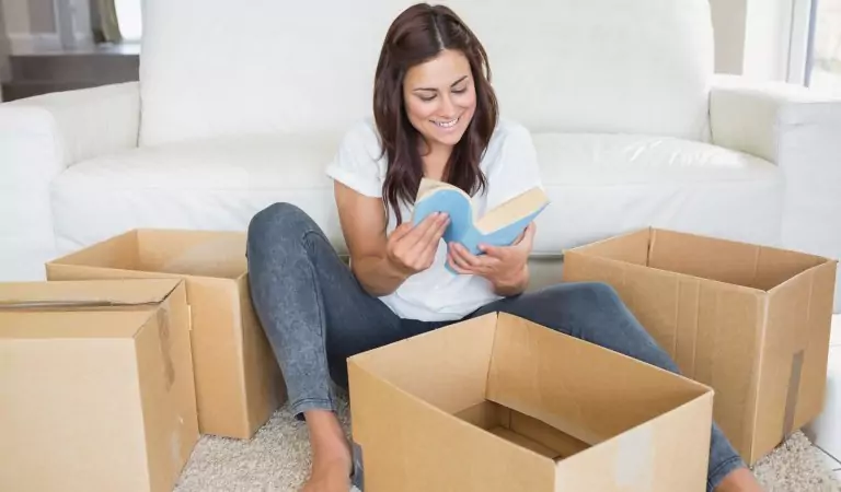 woman reading a book while sitting on the floor with some cardboard boxes