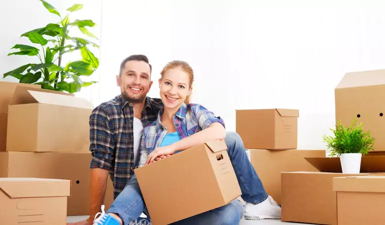 couple sitting on the floor with some cardboard boxes and a plant at back
