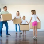 A family in a big empty room and each of them holding boxes